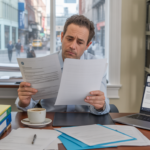 Chef d’entreprise examinant des documents administratifs dans un bureau lumineux et réaliste pour illustrer les démarches de modification ou fermeture d’entreprise.
