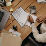 Focused woman calculating figures at office desk with a laptop and documents.