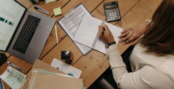 Focused woman calculating figures at office desk with a laptop and documents.